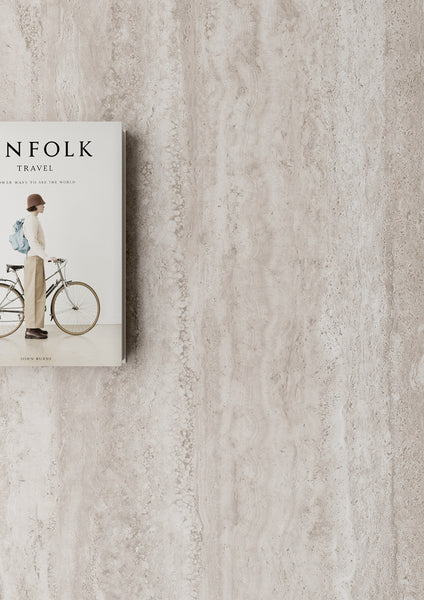 A book titled Kinfolk Travel with a cover image of a person standing beside a bicycle, placed on a light beige textured surface with ample empty space to the right.