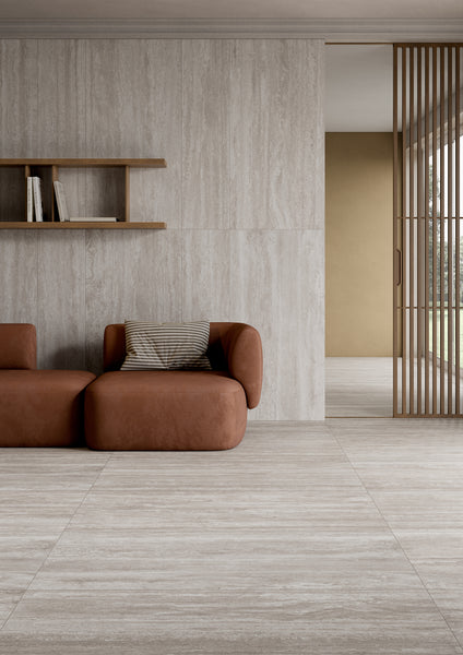 Minimalist living room with beige stone tile floors and walls, a brown modern sofa with a striped cushion, wooden shelving with a few books, and vertical wooden slats dividing the space.