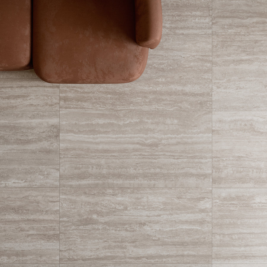 A top-down view of a brown upholstered sofa on beige stone-tiled flooring, with the sofa positioned in the upper left corner and most of the image showing the floor.
