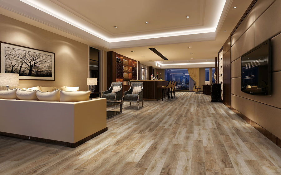 Spacious, modern living room with wood flooring, beige sofas, wall art, and warm lighting. An open kitchen with bar stools is visible in the background, and large windows reveal a cityscape at night.
