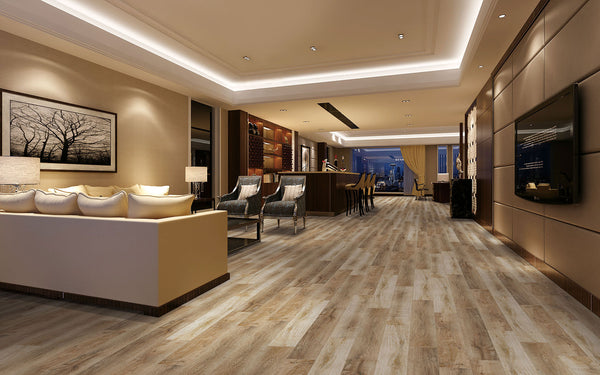 Spacious, modern living room with wood flooring, beige sofas, wall art, and warm lighting. An open kitchen with bar stools is visible in the background, and large windows reveal a cityscape at night.