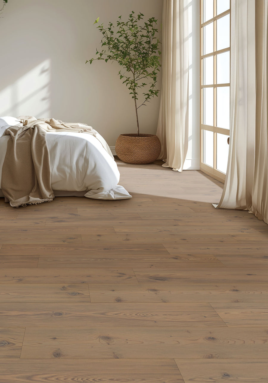 Minimalist bedroom featuring Glacial Isle 8 11/32" Waterproof Laminate flooring in light wood, a bed with white linens and beige blanket, sheer curtains, sunlit large windows, and a potted plant. The space feels calm and airy.