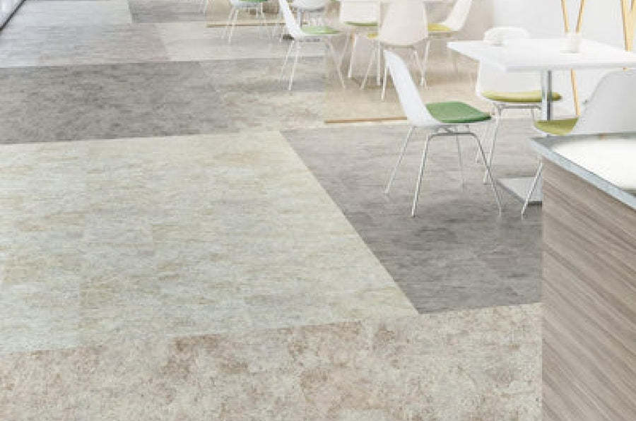 Modern cafeteria with white tables and chairs, some with green seat cushions, on Commercial Vinyl flooring in neutral tones. The clean, well-lit space features a minimalistic design and a patterned tile look.