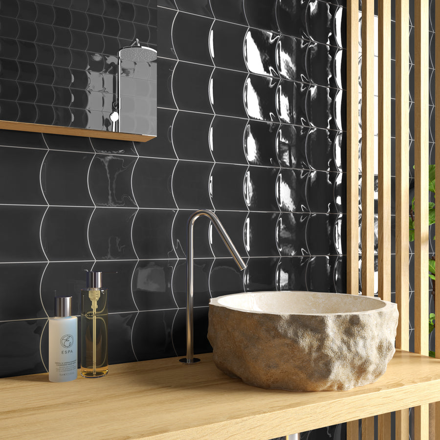 A modern bathroom vanity with a stone basin, sleek metal faucet, black wavy tile backsplash, and two bottles on a wooden countertop, with vertical wooden slats on the right side.