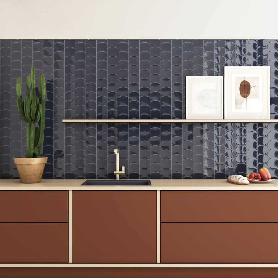 Modern kitchen with matte brown cabinets, beige countertop, and navy blue scallop-tile backsplash. A potted cactus, two framed artworks, and vegetables are displayed on the counter and floating shelf.