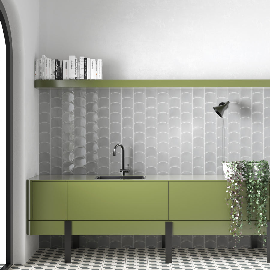 Modern minimalist kitchen with green cabinets, a gray scallop-tiled backsplash, open green shelf with books, a black lamp, and a hanging plant. The floor has a black and white geometric pattern.