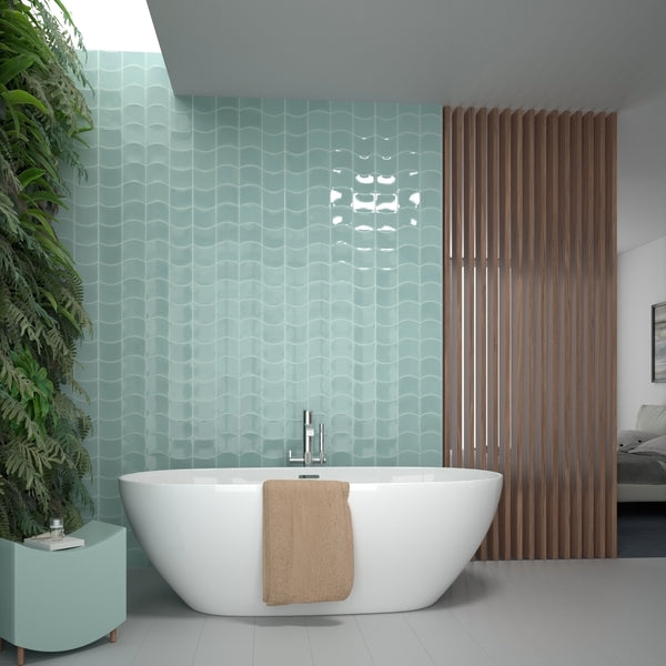 Modern bathroom with a white freestanding tub, a tan towel draped over the edge, light blue wavy tiles on the wall, indoor plants on the left, and wooden slats separating the bathroom from a bedroom.