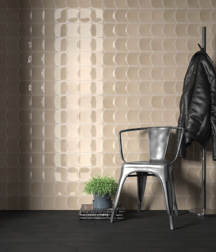 A metallic chair and a potted plant sit on a dark floor next to books and a coat rack with a black jacket, against a beige, textured, glossy tiled wall.
