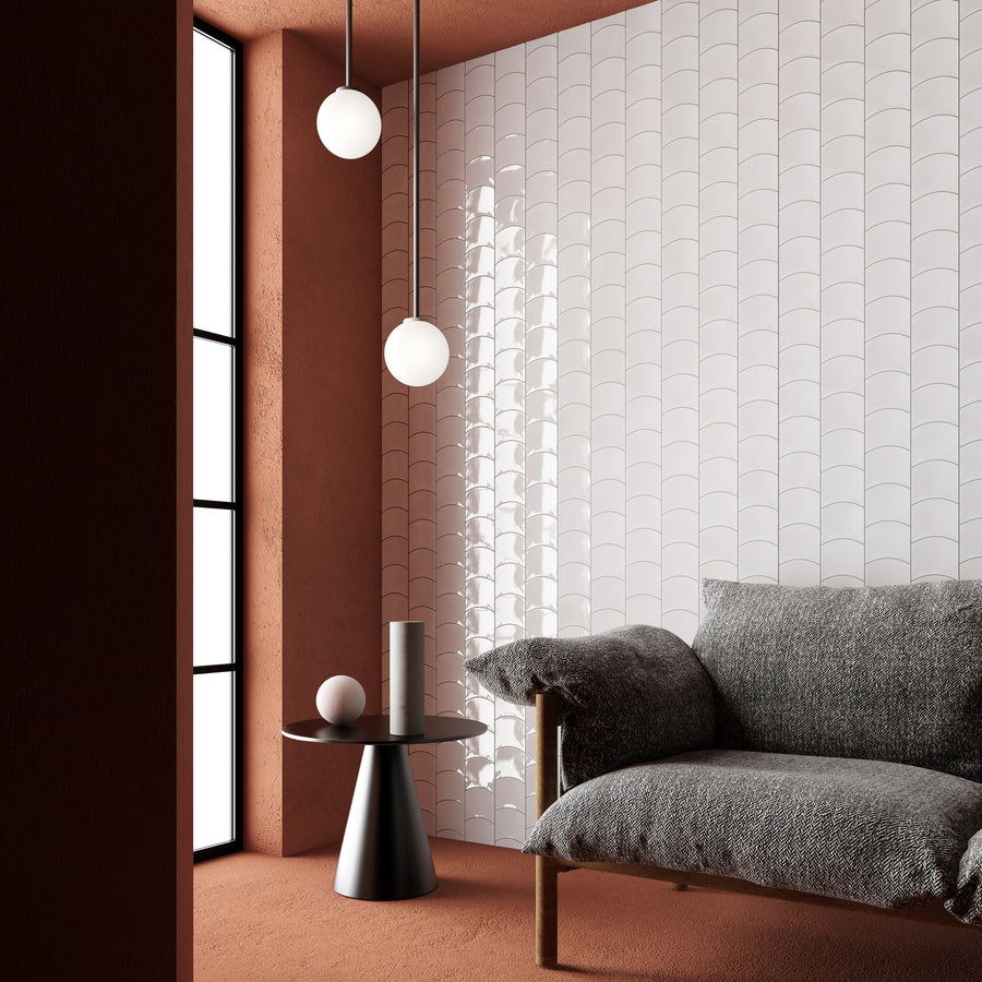 A modern, minimalist room with terracotta walls and carpet, a textured gray sofa, a small round black side table, two white pendant lights, and a white scalloped accent wall near a tall window.