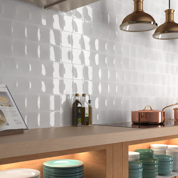 A modern kitchen with a glossy white textured tile backsplash, a wooden countertop, copper cookware, bottles of oil, cookbooks, and neatly stacked dishes in open shelves below.