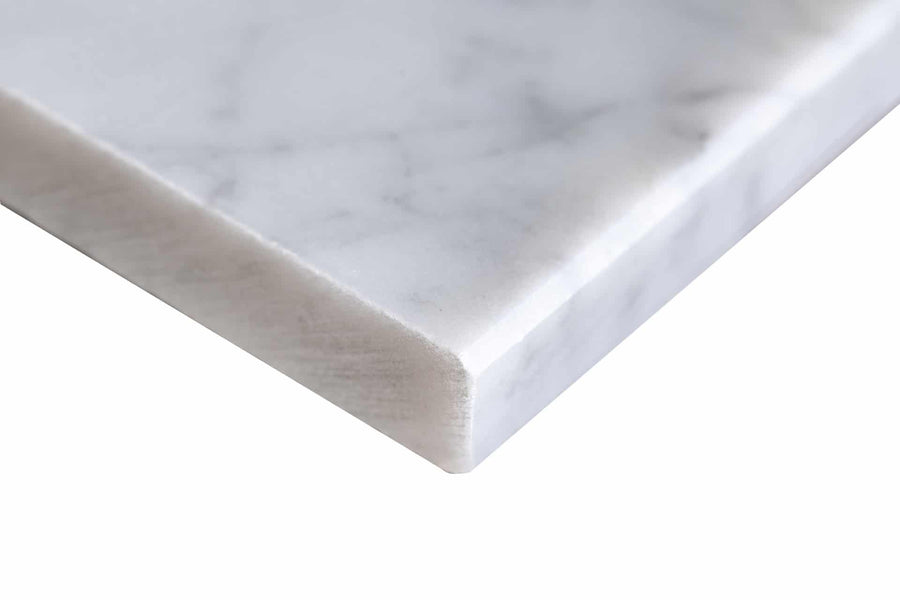 Close-up of the corner of a white marble slab with light grey veining, showing a smooth, polished surface and slightly rounded edge against a white background.