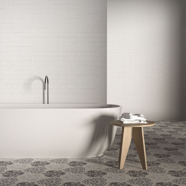 Minimalist bathroom with a white standalone bathtub, tall silver faucet, patterned black and white tile floor, and a small wooden stool holding folded white towels against a white tiled wall.
