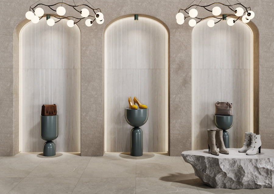 A modern boutique interior with three arched alcoves displaying fashion items—boots and handbags—on sculptural pedestals. A stone display table holds more boots. Overhead, unique branch-like light fixtures hang.