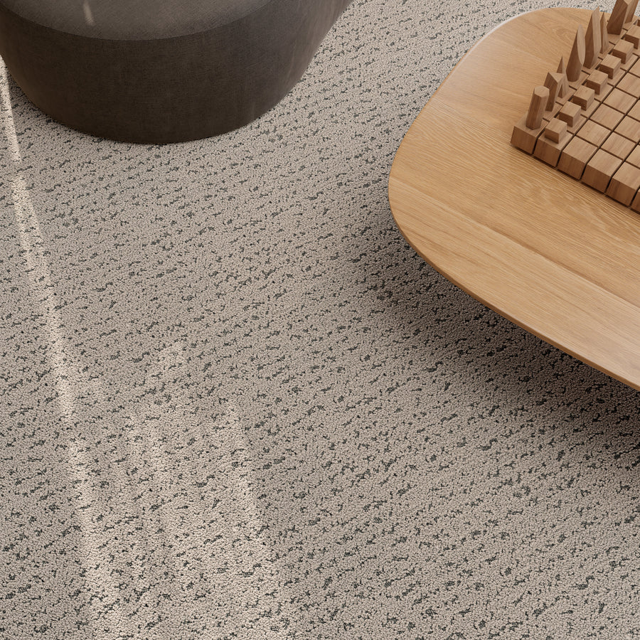 A close-up view of a textured, light-colored carpet with a subtle dotted pattern, next to a curved gray seat and a wooden table featuring a geometric wooden puzzle.