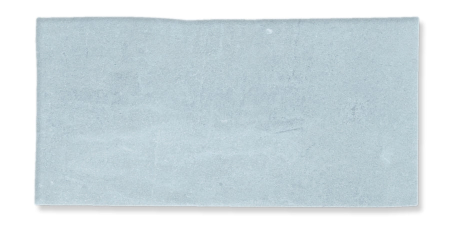 A rectangular, light blue tile with a slightly uneven surface and a soft, matte finish. The edges are straight with a subtle irregularity, and the color is uniform with faint variations.