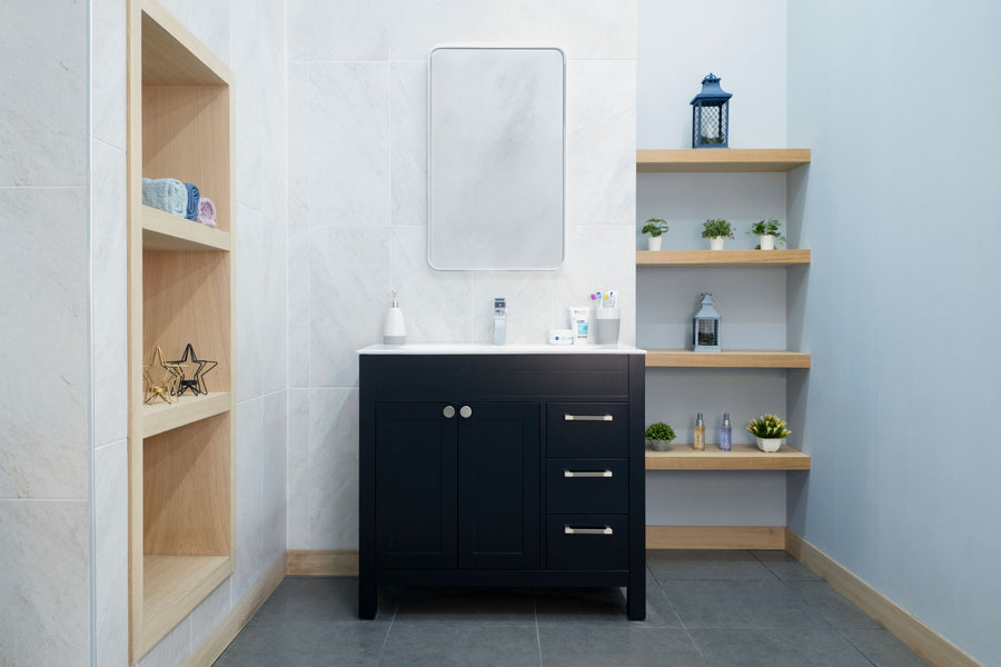 A modern bathroom showcases the Aria 36" Vanity in a sleek black finish with a white countertop, paired with a rectangular mirror, built-in wooden shelves for décor and plants, set against white and light blue walls.