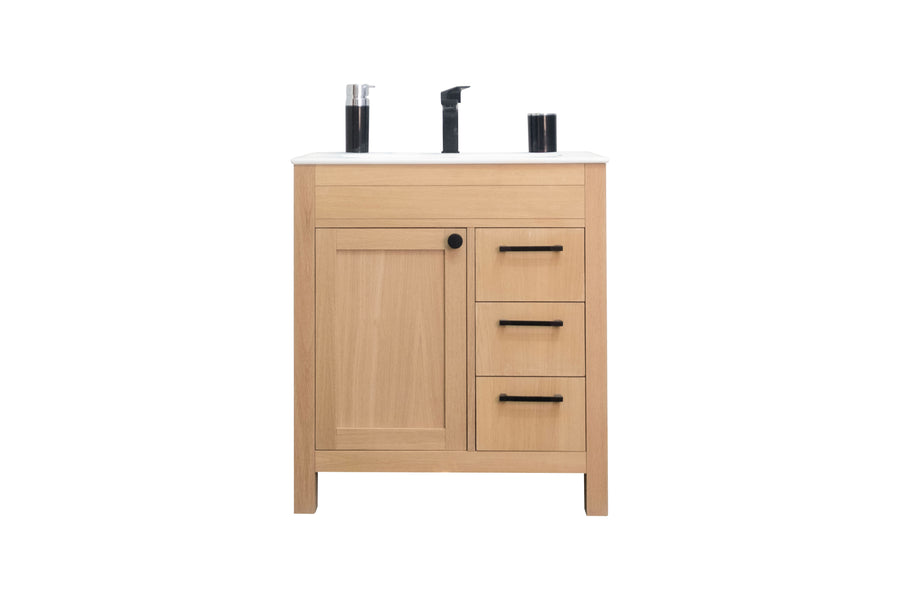 Light wood bathroom vanity with a white countertop, black faucet, and black hardware. Vanity features one cabinet door on the left and three drawers on the right. Two soap dispensers sit on the countertop.