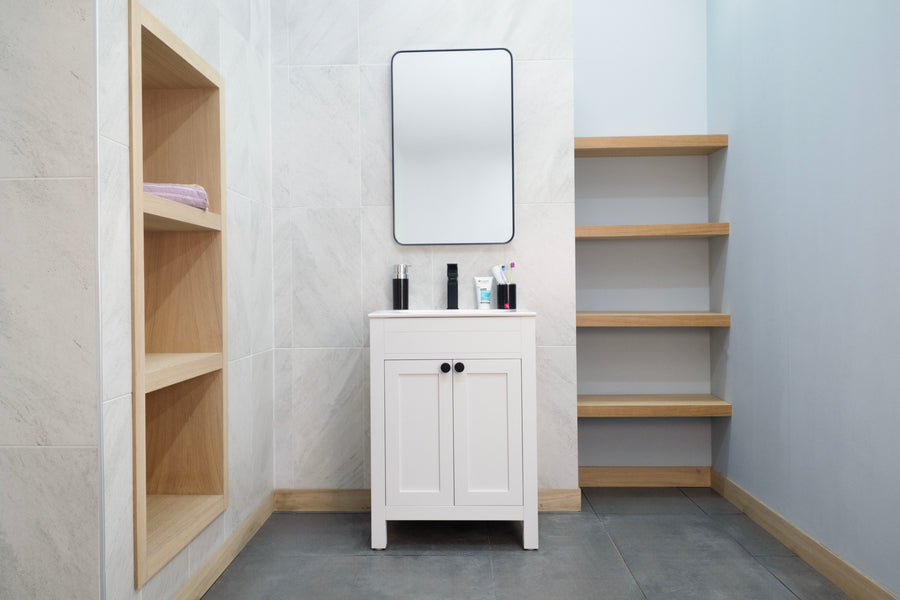 A modern bathroom with a transitional look includes the Aria 24" Vanity in white, a rectangular mirror, towel-filled built-in shelves on the left, and open wooden floating shelves on the right against light tiled and painted walls.