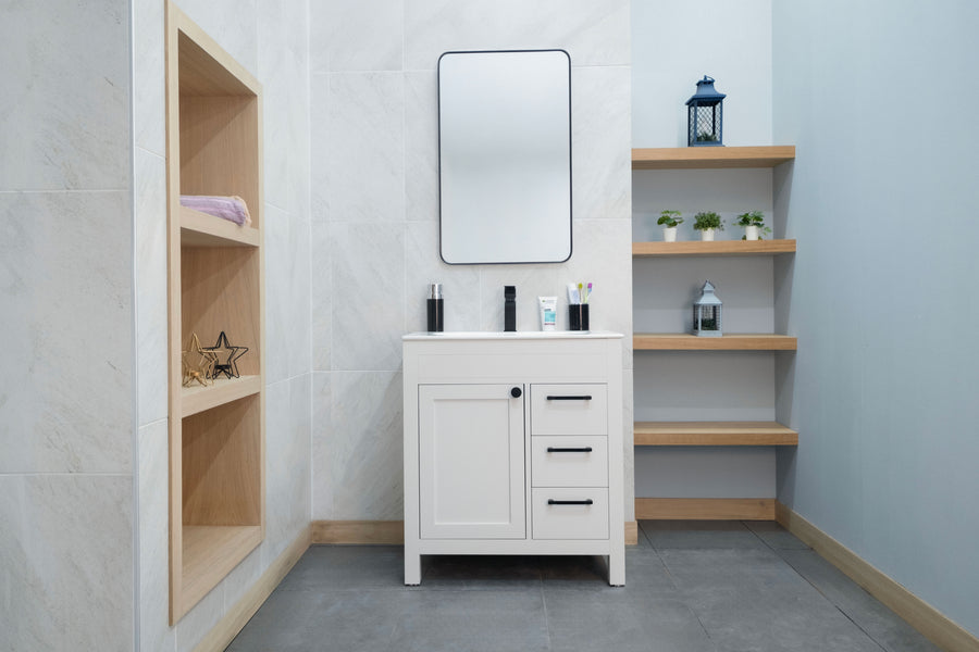 A modern bathroom features the Aria 30" Vanity, a rectangular mirror, open shelves with decor, built-in wall shelving for towels and ornaments, light walls, and gray tile flooring for a sophisticated touch.