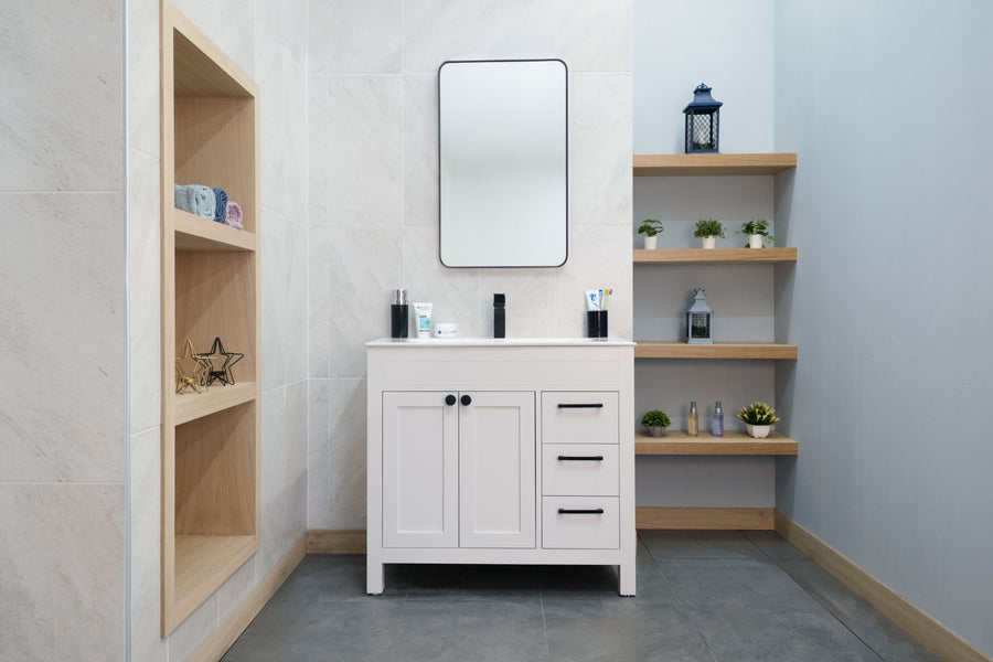 A modern bathroom with the Aria 36" Vanity and black handles, a rectangular mirror above, wooden shelves with decor on the left, and three floating shelves displaying plants and toiletries on the right.