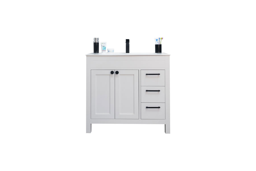 A white bathroom vanity with two cabinet doors, three drawers with black handles, and assorted toiletries including bottles and toothbrushes on top, shown against a plain white background.