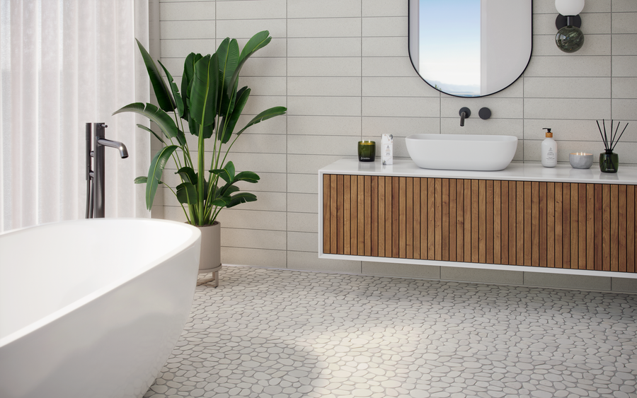 Modern bathroom with a white freestanding tub, a vanity with wood paneling, a round mirror, a potted plant, and pebble-style tile flooring. Natural light streams in through sheer curtains.