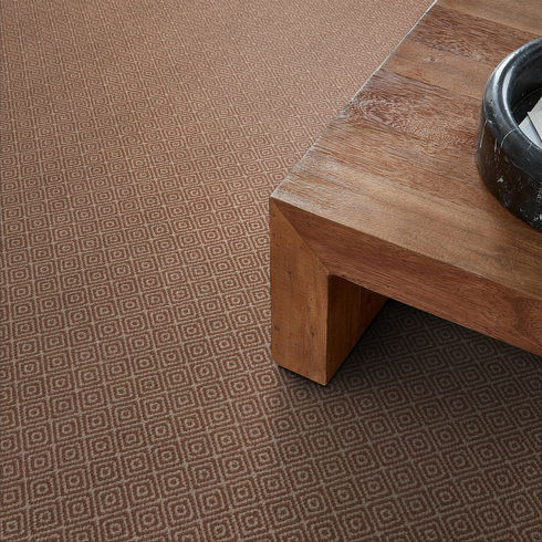 A close-up view of a wooden table with a black bowl on top, set on a brown carpet with a repeating geometric diamond pattern.