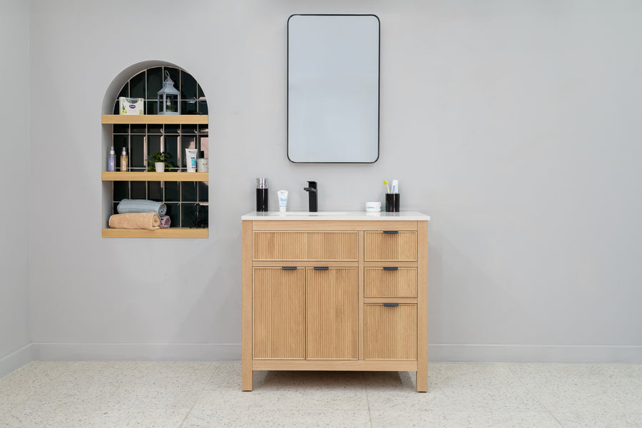 Minimalist bathroom featuring the light wood Catalina 36" Vanity with a white countertop and rectangular mirror. An arched shelf on the left showcases toiletries and decor, set against dark green tiles for transitional flair.