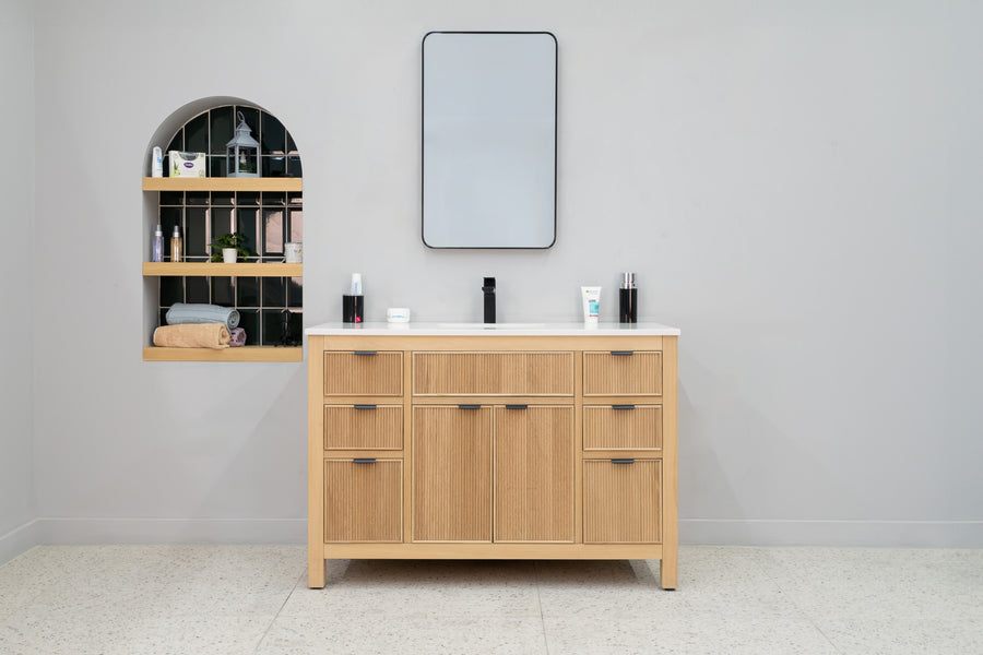 A modern transitional bathroom showcases the Catalina 48" Vanity with a white countertop, paired with a rectangular mirror, black faucet, and an arched wall shelf for toiletries and decor against light gray walls.
