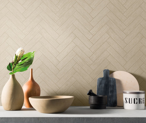 A minimalist kitchen counter displays ceramic vases, a wooden bowl, a mortar and pestle, black and white cutting boards, and a canister labeled SUCRE, against a beige herringbone-patterned wall.