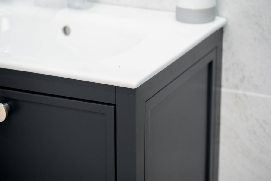 Close-up of a modern bathroom vanity with a black cabinet and a white countertop, featuring a silver knob and set against a light-colored tiled wall.