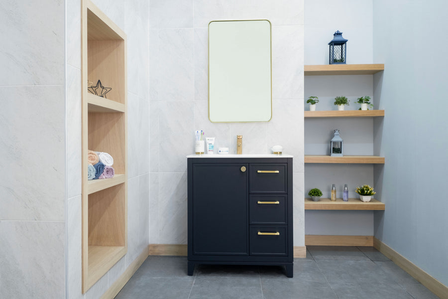 A modern bathroom with light walls, the Frame 30" Vanity with gold handles, a rectangular mirror, wooden shelves displaying plants and toiletries, plus a built-in shelf holding rolled towels and decor.