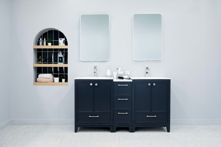 A modern bathroom features two Frame 60" Vanities with white countertops, double sinks, and rectangular mirrors. Towels and toiletries are stored in an arched wall niche with shelves. The walls are painted light gray.