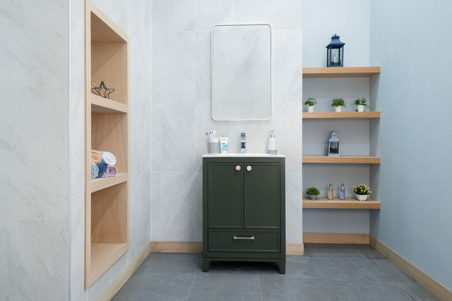Modern luxury bathroom with gray tile floor, the Frame 24" Vanity in olive-green topped by a mirror, toothbrushes, and soap dispensers. Wooden shelves hold potted plants, a lantern, and towels against light gray and blue walls.