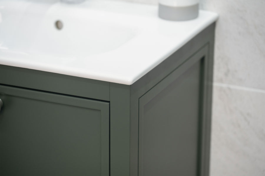 A close-up of a dark green bathroom vanity with a white countertop and sink, set against a light-colored tiled wall.