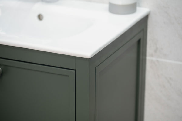 A close-up of a dark green bathroom vanity with a white countertop and sink, set against a light-colored tiled wall.