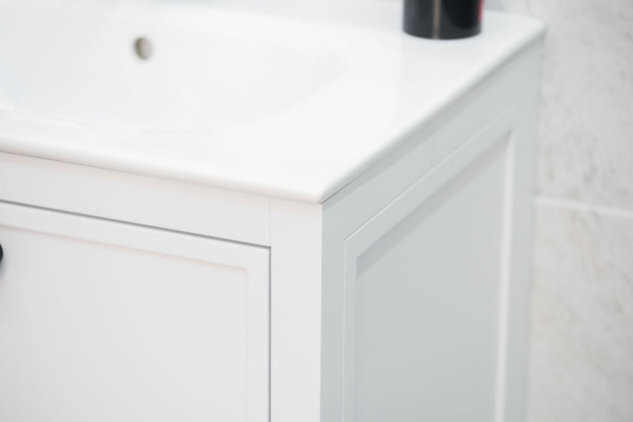 Close-up of the corner of a white bathroom vanity cabinet with a glossy sink on top, placed against a tiled wall. A black bottle is partially visible on the sink.