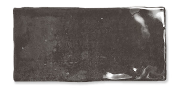 A rectangular, glossy black ceramic tile with slightly uneven edges and subtle reflections on its surface.