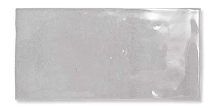 A rectangular, glossy, light gray ceramic tile with a slightly uneven surface and subtle reflections.