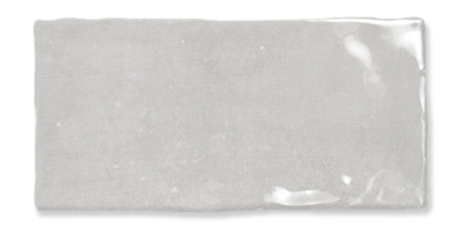 A rectangular, light gray ceramic tile with a glossy, reflective finish and slightly uneven edges.