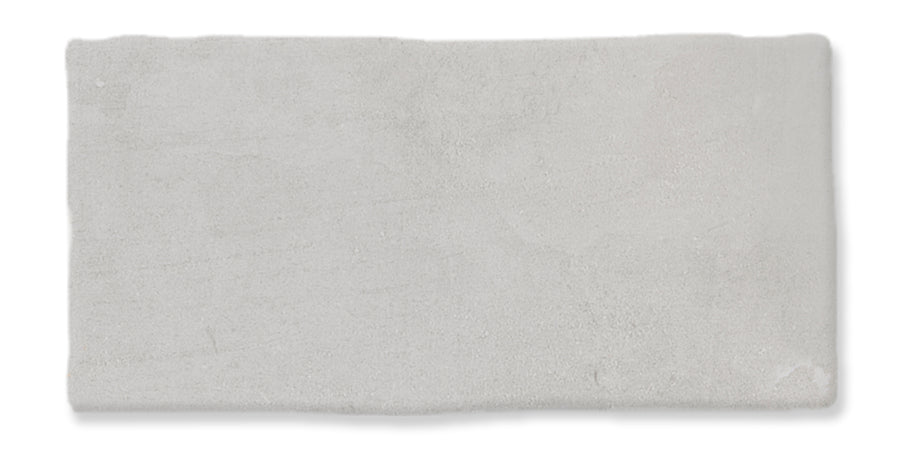 A rectangular, light gray tile with slightly uneven edges and a smooth, matte surface. The texture appears subtle and soft, with minor variations in shading.