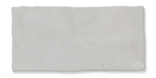 A rectangular, light gray tile with slightly uneven edges and a smooth, matte surface. The texture appears subtle and soft, with minor variations in shading.