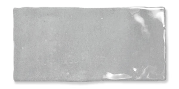 A rectangular, glossy light gray ceramic tile with uneven edges and a slightly reflective surface.