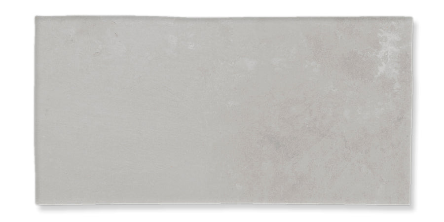 A rectangular, light gray ceramic or stone tile with a subtle, slightly mottled texture and an uneven, natural finish.