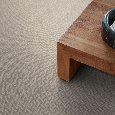 A close-up view of a wooden table with a black bowl on top, placed on a beige carpet with a subtle diamond pattern.