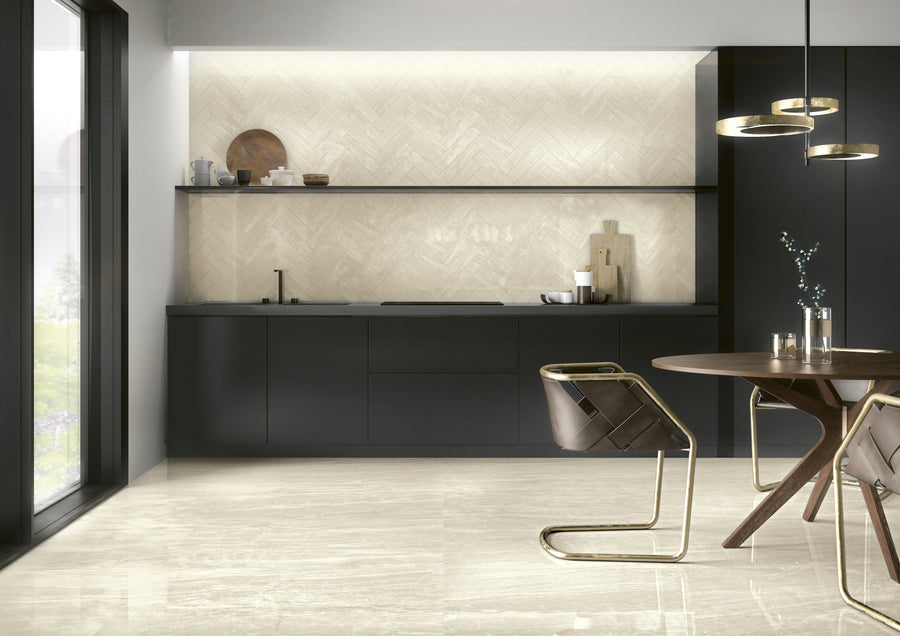 Modern kitchen with matte black cabinets, light herringbone backsplash, and open shelving. A round wooden table with gold and brown chairs is in the foreground, under a contemporary circular light fixture.