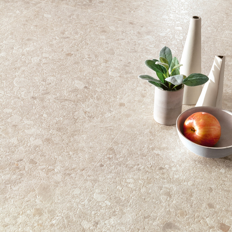 A beige stone tile floor with a small plant in a white pot, two tall white vases, and a white bowl holding a red apple arranged on top.