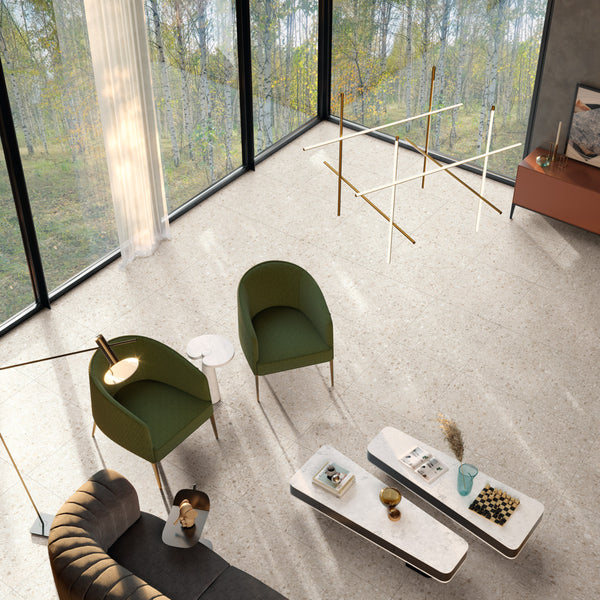 A modern living room with large windows showing a forest view, two green chairs, a curved gray sofa, minimalist coffee tables, and a geometric chandelier hanging from the ceiling.