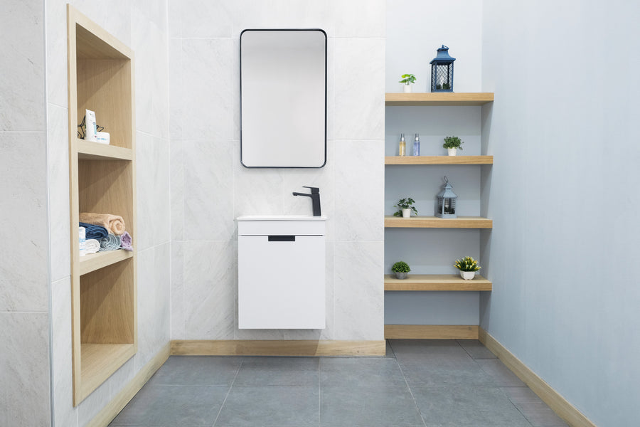 Minimalist bathroom with a floating white Luca 20" Vanity and black faucet under a rectangular mirror. Open shelves display towels and decor. The gray tile floor and light-colored walls create a contemporary look.