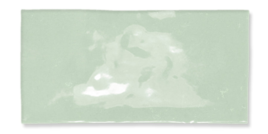 A rectangular, glossy, light green ceramic tile with subtle color variations and a slightly uneven surface texture.